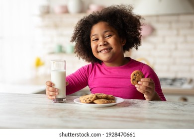 Tasty Snack. Cheerful Cute Black Girl Eating Cookies And Drinking Milk In Kitchen, Adorable Little Child Sitting At Table And Having A Bite With Healthy Calcium Drink And Homemade Pastry, Closeup - Powered by Shutterstock