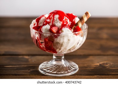 Tasty Sweet Dessert Of Ice Cream Poured With Berry Sirup In Glass Ramekin On Wooden Table. From Above. Unfocused Background