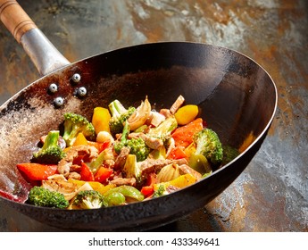 Tasty vegetable dish with broccoli and colorful peppers cooked in oil stained asian wok recipe against a rustic background