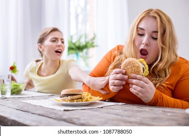 So tasty. Weak-willed overweight woman eating a sandwich and her friend stopping her
