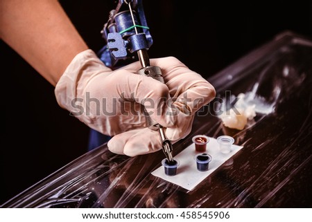Tatoo master is holding a tatoo machine and dip it into inks for tatooing/wizard tattoo salon / interesting profession