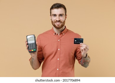 Tatooed young brunet man 20s with short haircut wears apricot shirt hold wireless modern bank payment terminal to process acquire credit card payments isolated pastel orange background studio portrait - Shutterstock ID 2017706894
