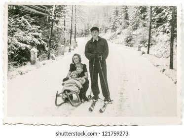 TATRAS MOUNTAINS, POLAND, CIRCA 1954 - Vintage photo of skier posing with her wife and little children on sled in snowy landscape, Tatras, Poland, circa 1954