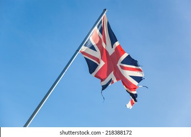 Tattered British Flag In Front Of The Blue Sky. Concept For Separatism Or Collapse Of Great Britain