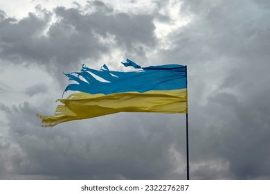 Tattered shabby Ukraine flag on gray cloudy sky as symbol of nation struggle and courage