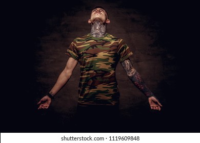 Tattoed young guy in a military t-shirt pose at the studio. Isolated on dark textured background. - Shutterstock ID 1119609848