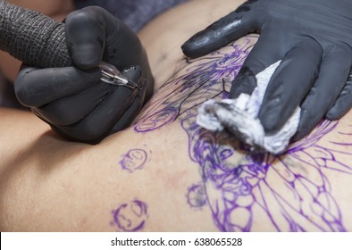 Tattoo Artist Applies Tattoo To The Shoulder Blade Of A Woman. She Is Cover An Old Tattoo With A New One