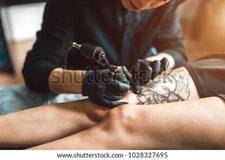 Tattoo artist in black gloves making a tattoo on the foot girls. Sterile.