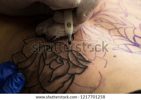 The tattoo artist creates a tattoo on the girls. Close-up.