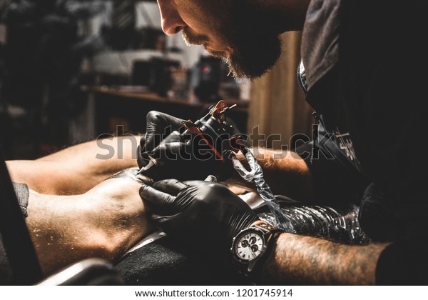タトゥーアーティストは 男性の体に絵を描く 刺青の機械と手の接写 の写真素材 今すぐ編集