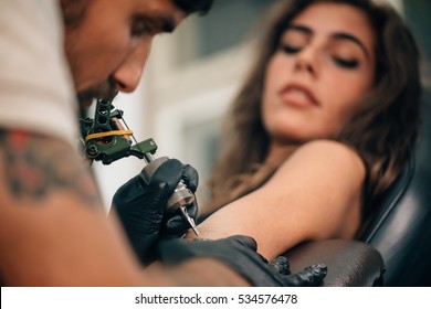 Tattoo artist creating a tattoo on a girl's arm. Focus on tattoo machine - Shutterstock ID 534576478