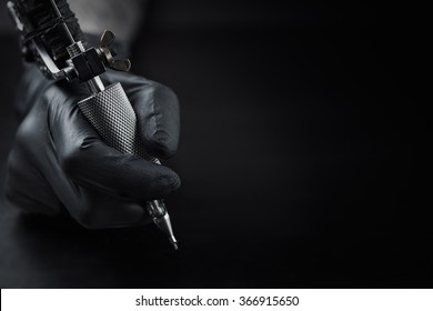 Tattoo artist holding tattoo machine on dark background with space for text
