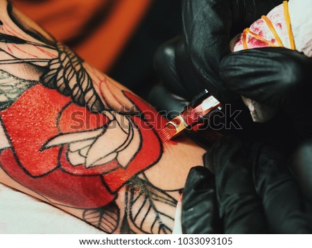 Tattoo artist at work. Woman in black latex glove tattooing a young man's hand with colorful picture in studio. Macro.