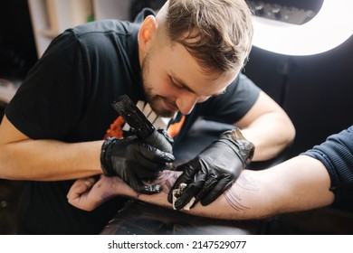 Tattoo master is tattooing a man's hand. Wireless tattoo machine, safety and hygiene at work. Close-up of tattoo artist work. Tattoo salon - Shutterstock ID 2147529077
