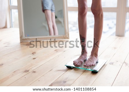 Tattoo on leg. Close up of skinny anorexic woman with tattoo on leg standing on weight scales Imagine de stoc © 