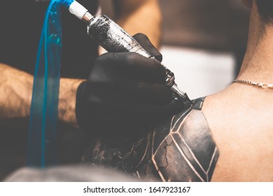 Tattoo salon. The tattoo master is tattooing a man on his shoulder. Tattoo machine, safety and hygiene at work. Close-up, tinted, tattooist. - Shutterstock ID 1647923167