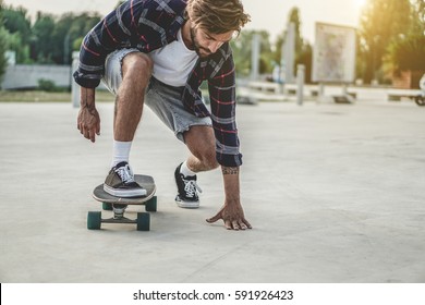 Tattoo skater performing with longboard at sunset in urban city square - Yong trendy man having fun with skateboard - Extreme sport concept - Focus on left hand and right foot - Powered by Shutterstock