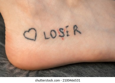 Tattoo With Words Loser, Lover And Heart On Woman's Foot In Red And Black Colours, Closeup View. Romantic Tattoo Symbol Of Youth Love And Disappointment In Life.