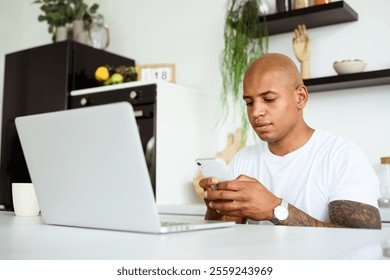 Tattooed african american man using smartphone near laptop and cup in kitchen	 - Powered by Shutterstock