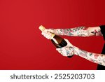 Tattooed arms of a person opening a champagne bottle. The champagne bottle is being opened by tattooed arms against a red background. Tattooed arms with champagne bottle