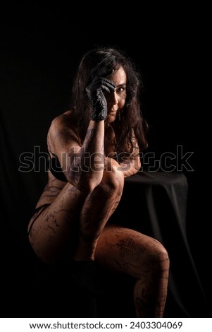 Tattooed artist, sitting, with painted and tattooed body against black background