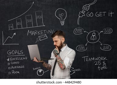 Tattooed Bearded Techer With Laptop Over School Desk With Formulas.