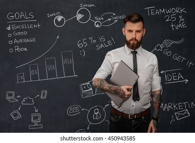 Tattooed Bearded Techer With Laptop Over School Desk With Formulas.