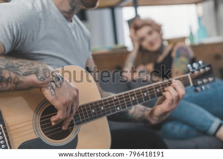 tattooed boyfriend playing on acoustic guitar for his girlfriend at home