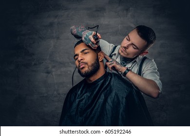 Tattooed Caucasian Male Barber Cutting The Beard To Black Stylish Man.