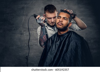 Tattooed Caucasian Male Barber Cutting The Beard To Black Stylish Man.