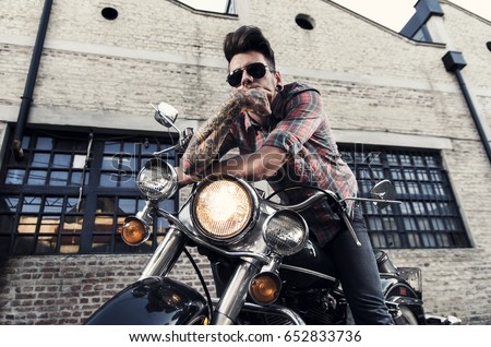 Tattooed cool young man with sunglasses sitting on vintage motorcycle  