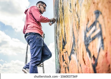 Tattooed graffiti writer painting with color spray on the wall - Contemporary artist at work - Urban lifestyle,street art concept - Focus on his face and hand can