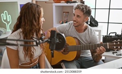 A tattooed man with a guitar smiling at a woman by a microphone in a bright, modern music studio. - Powered by Shutterstock