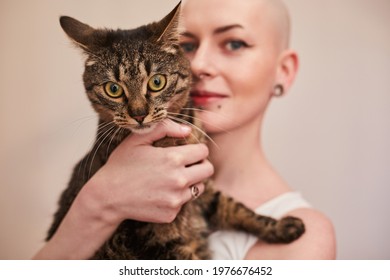 Tattooed Masculine Woman Posing In Front Of The White Wall With Her Striped Cat