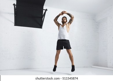 Tattooed And Muscular Athlete Doing Jumping Jacks Isolated On White Brick Wall Next To Black Pull Bar