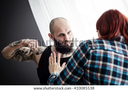 Tattooed muscular man beating his redheaded wife. Domestic violence