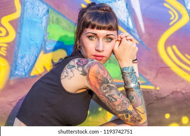 Tattooed Rebel Girl Posing Against A Wall Painted With Colorful Graffiti