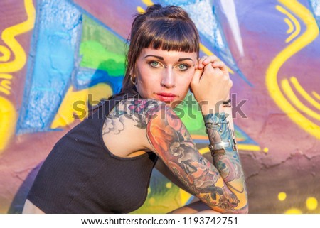 tattooed rebel girl posing against a wall painted with colorful graffiti