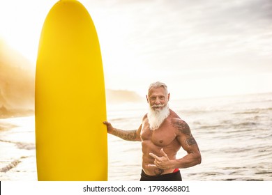 Tattooed senior surfer holding surf board on the beach at sunset - Focus on his face