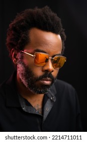 Tattooed Serious Black Male With Natural Afro Hair Style And Stylish Gold Mirrored Sunglasses Posing Under Red Light And Dark Background