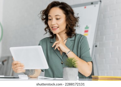 Tattooed speech therapist pointing at chin during video call on digital tablet in consulting room - Shutterstock ID 2288172131