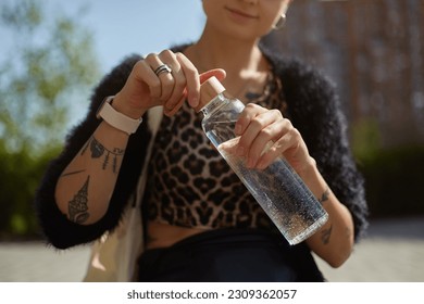 Tattooed young woman opening a glass bottle in close up. Diverse female person drinking fresh water outdoor. Sustainability and diversity concept - Powered by Shutterstock