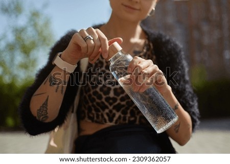 Tattooed young woman opening a glass bottle in close up. Diverse female person drinking fresh water outdoor. Sustainability and diversity concept Foto stock © 