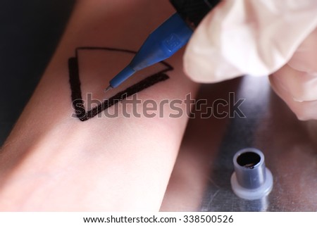 Tattooist draws triangle on the woman's arm, close up