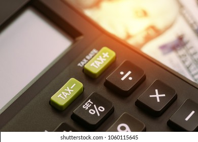 Tax cuts or reduce concept, selective focus on TAX minus buttons on calculator with background of blurred US Dollar banknotes, United States government tax overhaul policy.