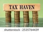 TAX HAVEN - words on a wooden block on a background of stacks of coins