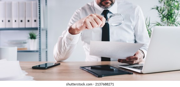 Tax inspector and financial auditor looking through magnifying glass, inspecting company financial papers, documents and reports, selective focus - Shutterstock ID 2137688271