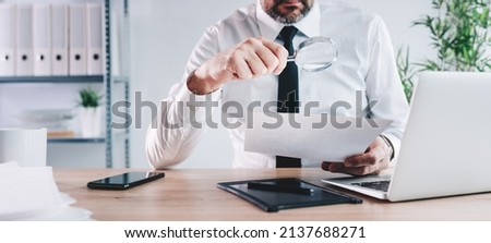Tax inspector and financial auditor looking through magnifying glass, inspecting company financial papers, documents and reports, selective focus