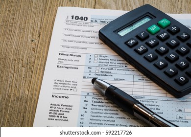 Tax preparation form US 1040 with calculator and pen on wooden table