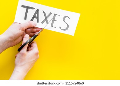 Tax Reduce Concept. Hands With Sciccors Cut Paper With Word Taxes On Yellow Background Top View Copy Space